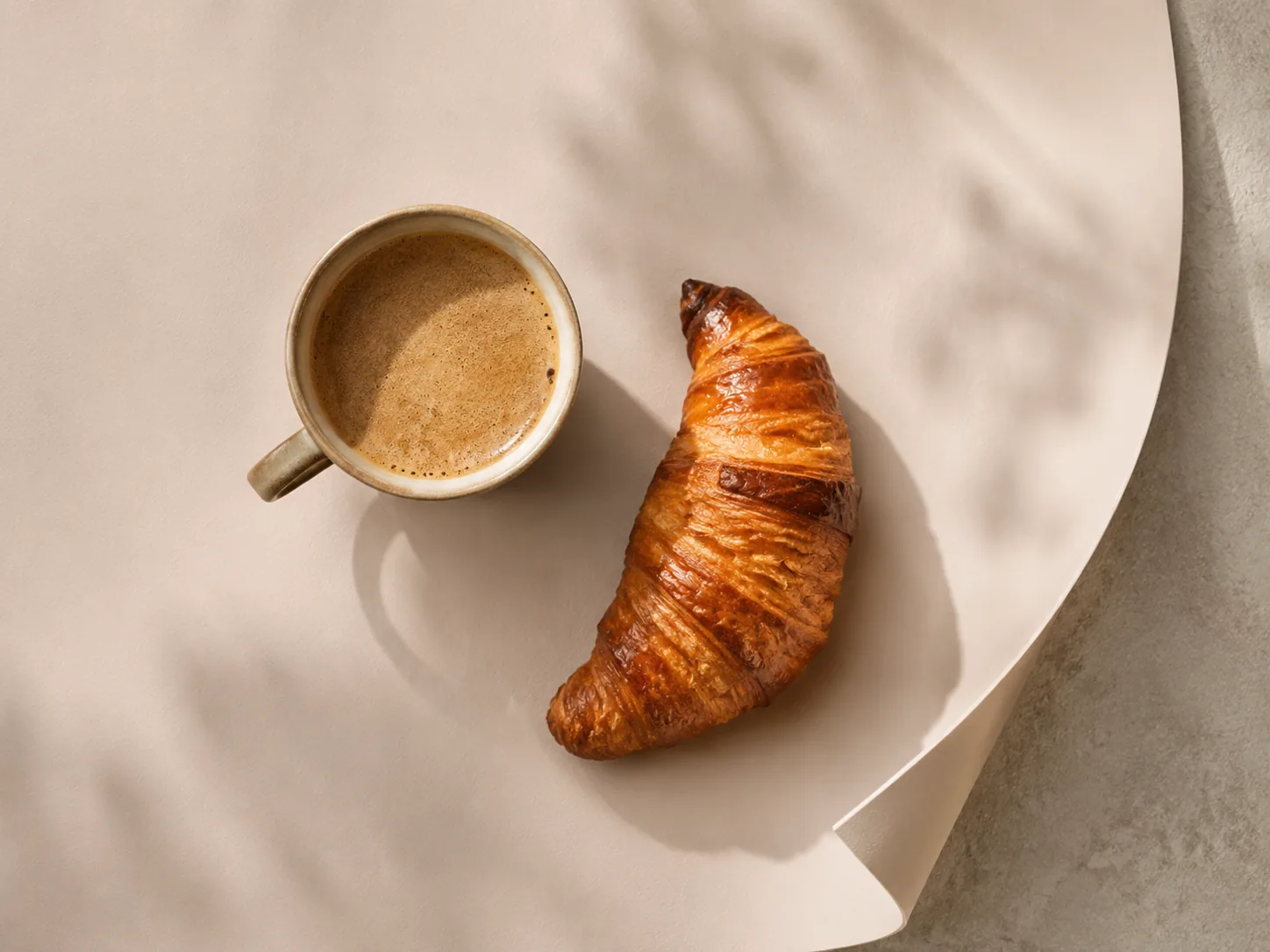 Overhead flat lay on pastel skin-feel paper with coffee and croissant